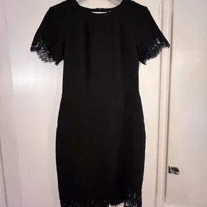 Svart kostymklänning - Den perfekta svarta klänningen, med lite tjockare kostymmaterial vilket sitter väldigt snyggt på. Dragkedja bak, slits nertill bak. Spetsdetaljer på ärmarna och längst ner. 