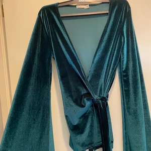 Smaragdgrön topp i sammet - Fin smaragdgrön topp från Nelly trend i sammet med knytning i midjan. Utsvängda trumpetärmar. Väldigt sparsamt använd så gott skick! 