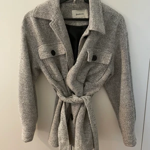 Grå Vår/Höstjacka från Stradivarius  - Gråmelerad Vår/Höstjacka från Stradivarius med bälte och svarta knappar. I mycket bra skick, som ny. Storlek S. 