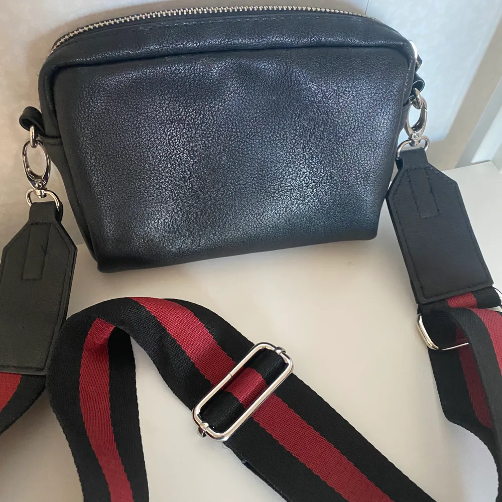 En liten handväska med avtagbar axelrem i svart/rött. Fuskskinn. Endast använd entaka gång.. Väskor.
