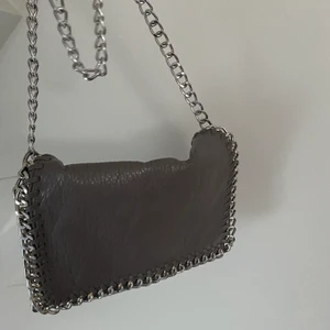 Grå väska  - Säljer min mccartney likande väska. Köpt på scorett för 500kr och säljer den för 180. Väskan har inga synliga fel och ser ut som ny. Finns fack med dragkedja inuti och ute på väskan, väldigt bekväm och passar med det mesta! ☺️ 