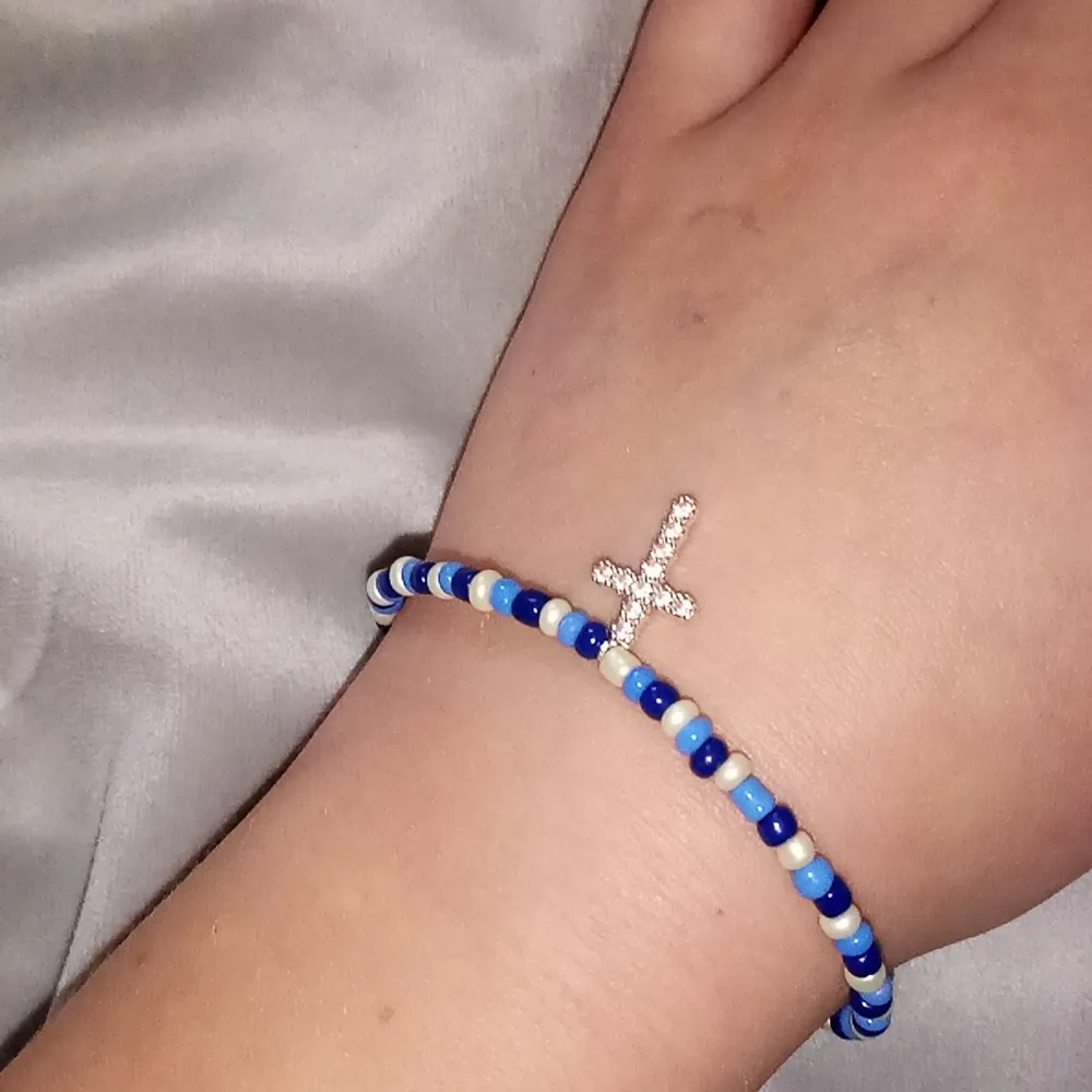 Ett armband gjort av elastisk tråd i vit och två olika nyanser av blå. Övrigt.