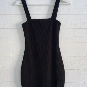 Svart klänning med slits - Svart klänning med slits, ribbat material. Aldrig använd då den är för liten för mig, prislappen sitter kvar