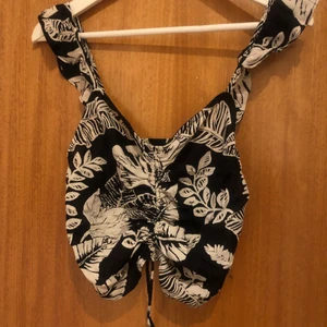 Svartvit linne stl S - En somrigt linne i svartvit med blommönster på. Är lätt i tyg och kan dra åt snörena för att anpassa längd. Passar en med mindre byst som är mellan s/m.  