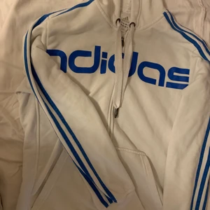 Adidas tröja - Vit adidas tröja med blåa streck. Storlek M men passar M-L. Står adidas med blått på bröstet och dragkedja. Luva. 