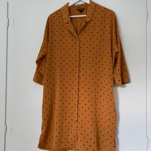 Prickig klänning från Monki - Senapsgul klänning med svarta prickar. Endast använd en gång. Strl XS, men är oversized.  En utav hylsorna till bältet är lite trasig, men går att använda som vanligt ändå eller enkelt sy dit igen.  Hämtas på plats eller skickas med post. Vill du ha den skickad tillkommer fraktkostnad på 45 kr (priset för postnords blå påse).