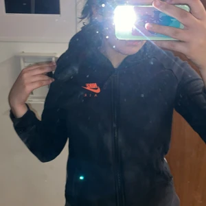 Svart/grå Nike kofta - En svart kofta med grått där bak och orange Nike märke