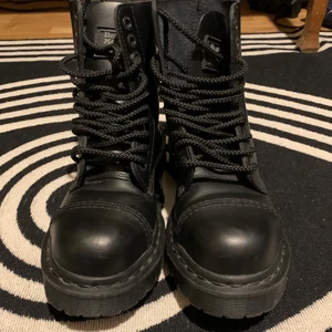 Dr Martins 10-håls (sällsynt modell) - SVARTA DR MARTENS MED STÅLHÄTTA 10-håls SKICK: Nästintill nyskick, kanske använts 1-2 ggr. Dessa köpte jag tidigt 2000-tal och det var en ovanlig modell då. Notera att de inte har den typiska gula sömmen! Älskar dessa kängor men nu har jag förvarat dom så länge och knappt använt dem så det är dags att släppa taget. Tvättade skosnören. MATERIAL: Blank läder. OBS: katt finns i hemmet. 