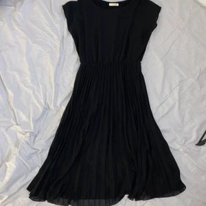 Svart klänning med plisserad kjol - Svart klänning med plisserad kjol som går till nedanför knäna. Väldigt skön och sitter fint. Använd ett fåtal gånger, inga skador eller fläckar. Såldes i onesize, passar ungefär S-L