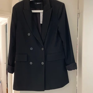 Oanvänd kavaj  - Oanvänd svart kavaj från Gina tricot, lappen finns kvar. Perfekt som kavaj eller sommarjacka då den är lite tjockare än en vanlig kavaj! 