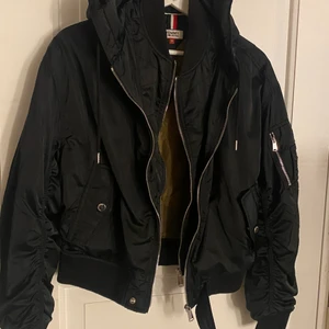 Tommy Hilfiger bomberjacka - Bomberjacka från tommy hilfiger med 2 dragkedjor. Använd men i väldigt fint skick. inga slitningar. Knappfickor samt en liten ficka med dragkedja på armen. Nypris 999kr