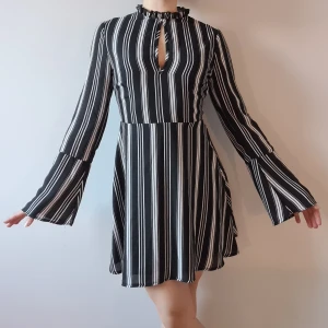 Svartvit randig klänning - Svartvit randig klänning i böljande material med dragkedja i ryggen. Volangkrage upptill. Öppen glipa vid bysten. Vida ärmar. Säljes då dem är för liten. Frakt tillkommer.