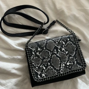 Väska - Snygg väska med ormskin motiv, minns inte var den är köpt. Den har dragkedja och bandet kan bli kort och långt. 