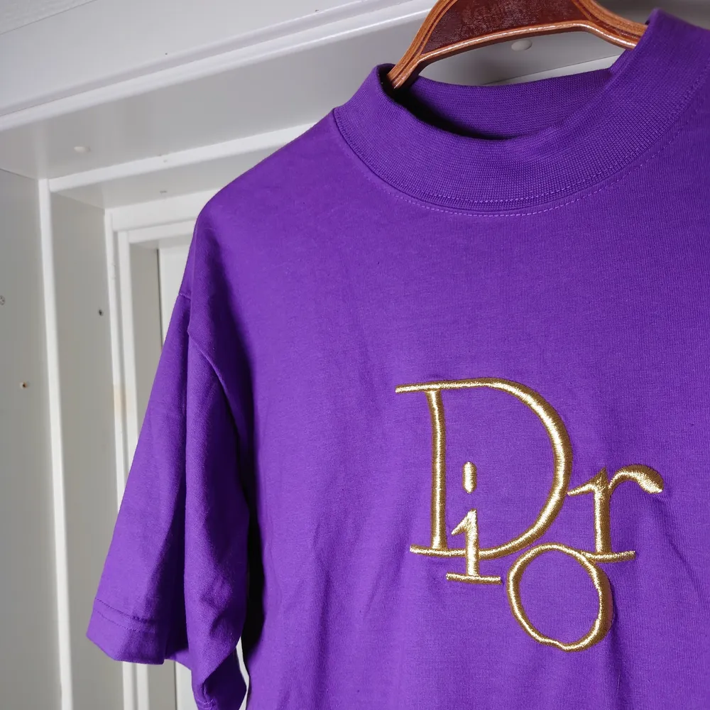Fejk Dior t-shirt i lila med guldlogga. Ingen storleksmärkning men bör vara M🍀. T-shirts.