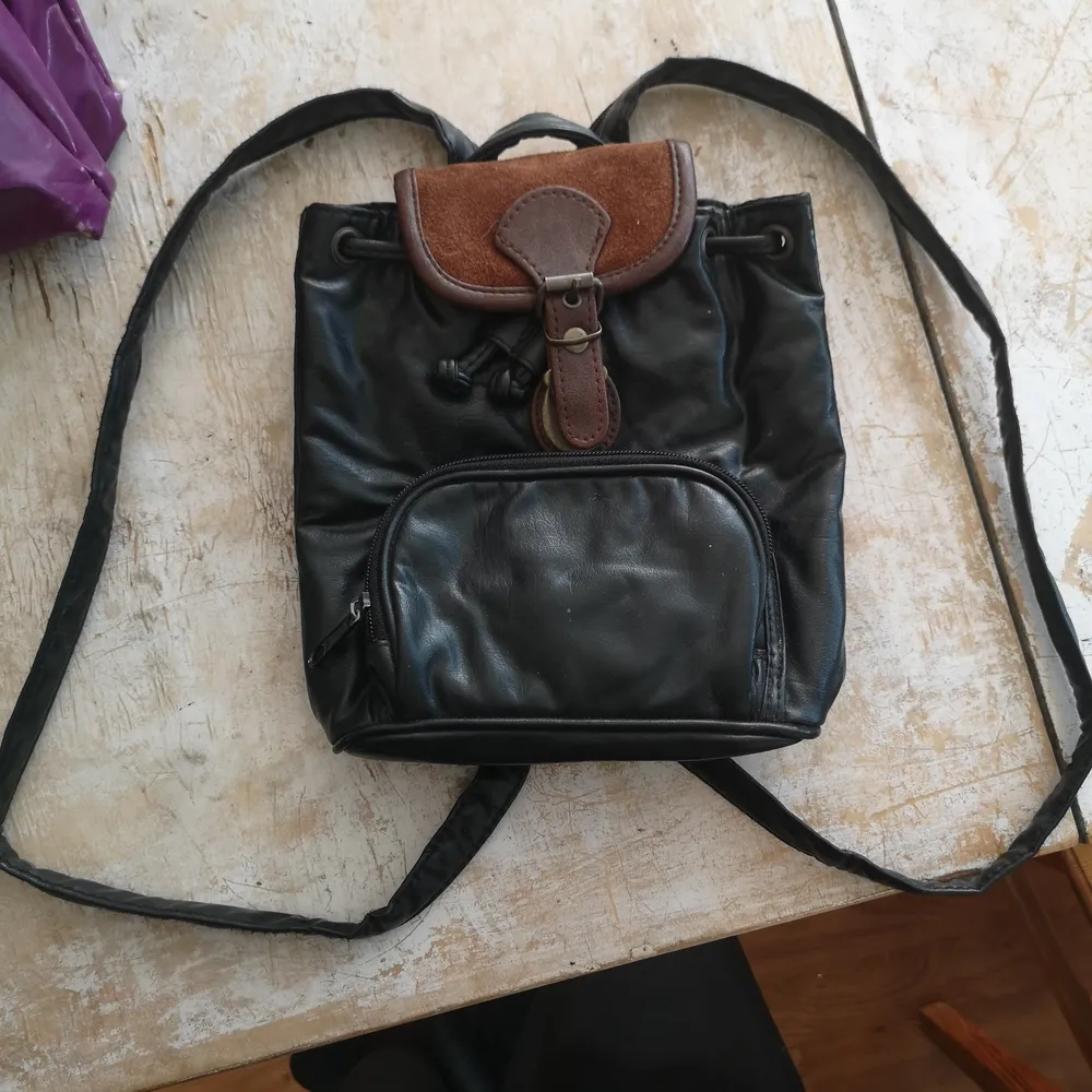 Liten svart läder ryggsäck med brun mocka detalj. Väskor.