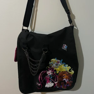 Monster high messenger bag - Cool messenger bag med monster high tryck och kedjor hängandes bredvid. Köpt på grund av trycket men användes bara 4/5 gånger. Bortsätt från den stora fickan har den också en mindre ficka på sidan av väskan vilket är synligt på andra bilden. Bandet är justerbart. 