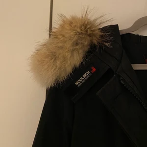 Woolrich vinterjacka! - Säljer min fina svarta Woolrich vinterjacka. Den har en äkta päls på luvan som även är avtagbar. Två fickor framtill och jackan knäpps med dragkedja alternativ med knappar. Woolrich märket vid luvan går även att knäppa fast undertill så det inte syns. Jackan är använd 2 vintrar men är ändå i väldigt bra skick, inga slitage. 🖤