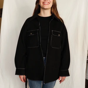 Svart jacka med vita sömmar och bälte - Svart jacka i skjort-modell. Vita sömmar. Bälte med knapp-detaljer och kedje hällor. Ursprungligen från H&M som är omgjord av Scannable UF. Genom att skanna en QR-kod som finns fäst på plagget kan du läsa mer om materialet och dess miljöpåverkan!✨✨