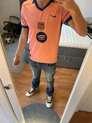 Barça rosa matchtröja Nike - Säljer en rosa FC Barcelona matchtröja från Nike med mörkblå detaljer och logga på bröstet. Tröjan har V-ringning, korta ärmar och är tillverkad i ett lätt, ventilerande material. Spotify-logga på framsidan och klassisk sportig design.
