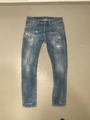 Dondup George - Säljer ett par blå skinny jeans från Dondup med slitna detaljer och distressed look. Jeansen har klassisk femficksmodell, knappgylf och är tillverkade i denim. Perfekta för en avslappnad och trendig stil.