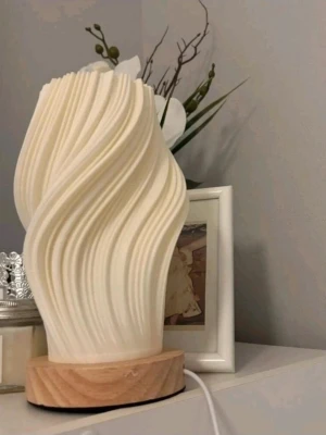 Modern vriden bordslampa i beige - Säljer en unik bordslampa med vriden design i beige plast och träbas. Lampan har ett organiskt, vågigt mönster som ger ett coolt ljusspel när den är tänd. Perfekt som dekorativ detalj i rummet och drivs med sladd. Ingen synlig logga eller märke.