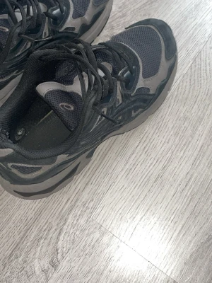 Svarta och grå Asics Nyc onyc gels - Säljer ett par svarta och grå sneakers från Asics med mesh- och mockadetaljer. Skorna har en chunky sula och klassisk Asics-logga på sidan. Perfekta för dig som gillar sportig och trendig stil. Sköna att gå i och passar till många outfits.