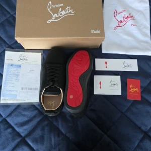 Christian Louboutin sneakers svarta - Exklusiva svarta sneakers från Christian Louboutin med ikonisk röd sula och diskret logga på innersulan. Skorna har snörning, rund tå och är tillverkade i skinn med detaljer i svart textil. Kommer med originalkartong, dustbag och äkthetskort.