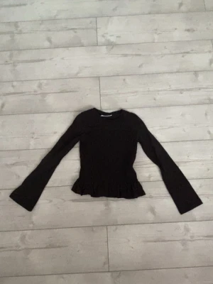 Svart topp med volang från Gina Tricot - Säljer en svart långärmad topp från Gina Tricot. Toppen har en figurnära passform och volangdetalj nedtill som ger en söt touch. Tillverkad i mjukt bomullsmaterial och passar perfekt till jeans eller kjol.