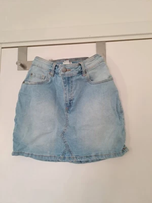 Ljusblå jeanskjol från Roxy - Säljer en ljusblå jeanskjol från Roxy med klassisk femficksmodell och knappgylf. Kjolen har en kort passform. Perfekt till sommaren och enkel att matcha med olika toppar. 