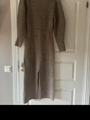 Beige stickad långklänning Adoore - Mysig beige stickad långklänning från Adoore med lång ärm och midja. Klänningen har en ribbad struktur och en snygg slits framtill som ger extra edge. Använd en gång. Som ny