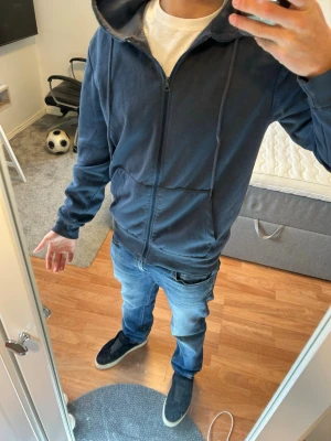 Mörkblå hoodie med dragkedja - Mörkblå hoodie med hel dragkedja framtill och huva. Klassisk passform med fickor på sidorna och ribbade muddar vid ärmar och nederkant. Perfekt för en avslappnad stil och enkel att matcha med jeans eller joggers.