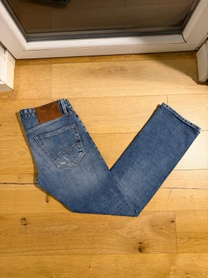 Replay Waitom jeans blå  - Snygga Replay Waitom jeans i klassisk blå tvätt med regular fit. Jeansen har fem fickor, slitna detaljer och läderpatch bak i midjan. Passar dig som gillar en avslappnad men stilren look. Materialet är slitstark denim i bomull. Uppskattat skick - 8.7/10 | Mvh ItsForfits 🌟