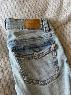 Ljusblåa Perfect Jeans från Gina Tricot - Snygga ljusblåa jeans från Gina Tricot, modell Perfect Jeans. Klassisk femficksdesign med knappstängning och bälteshällor. Jeansen har en tvättad look och är tillverkade i bomull med en skön passform.