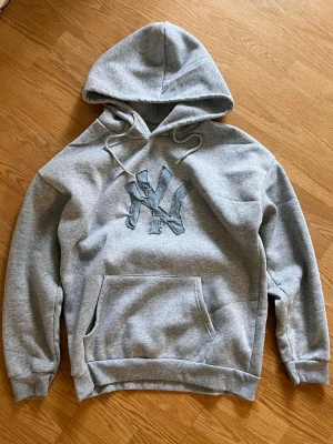 Grå hoodie med denim NY Yankees logga - Säljer en grå hoodie med en NY Yankees logga i denim gjord av mig. Loggan har en distressed look och hoodien är i storlek M