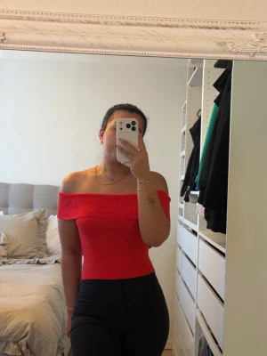 Röd offshoulder ribbad topp - Säljer en snygg röd offshoulder topp med ribbad struktur. Toppen är tight och har en bred krage som sitter över axlarna. Perfekt för dig som vill ha en trendig och stilren look. Materialet är mjukt och stretchigt, vilket gör den bekväm att bära.