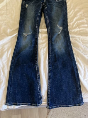 Mörkblåa jeans från Gina 14+ - Säljer ett par mörkblå bootcut jeans med snygga slitningar och ljusa tvättade partier. Jeansen har kontrastsömmar och utsvängda ben för en retrovibe. Perfekta för dig som gillar en avslappnad men trendig stil. Jättefina 💕helt nya 