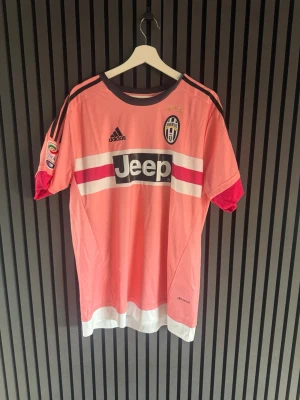 Juventus rosa matchtröja Pogba #10 - Juventus rosa matchtröja från Adidas med Pogba och nummer 10 på ryggen. Tröjan har Jeep-logga på bröstet, svarta och vita detaljer samt Serie A-märke på ärmen. Tillverkad i lätt funktionsmaterial, perfekt för fotboll eller samling.