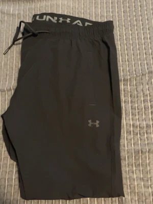 Svarta mjukisbyxor från Under Armour - Säljer ett par svarta mjukisbyxor från Under Armour med resårmidja och dragsko. Byxorna har diskreta fickor på sidorna och logga framtill. Perfekta för chill eller träning, tillverkade i ett mjukt och stretchigt material.