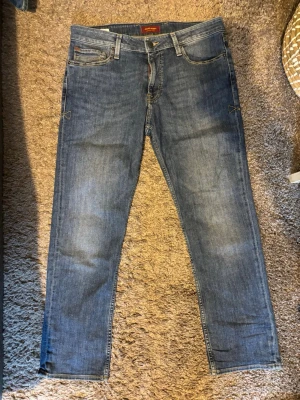 Clark jeans från Jack & Jones - Säljer ett par klassiska blå jeans från Jack & Jones med rak passform och fem fickor. Jeansen har en snygg tvättad look, bälteshällor och detaljerade sömmar. Tillverkade i bomull med en skön känsla och passar perfekt till din vardagsstil. Aldrig använd!