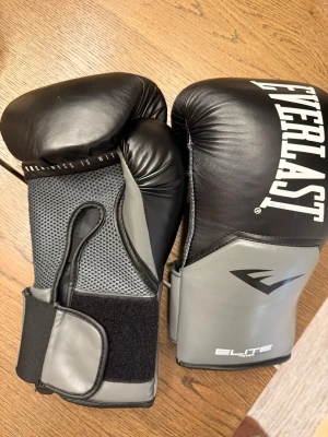 Svarta och grå boxningshandskar Everlast - Säljer ett par svarta och grå boxningshandskar från Everlast, modell Elite 16oz. Handskarna har kardborreknäppning och ventilerande mesh på handflatan för extra komfort. Perfekta för boxningsträning eller kampsport. Använda ca 10 gånger. 