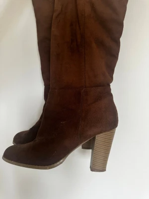 Bruna mockastövlar med klack - Snygga bruna stövlar i mocka med hög, bred klack och rundad tå. Stövlarna har en stilren design och är perfekta för dig som vill ha ett par trendiga boots med lite höjd. Materialet är mjukt och ger en lyxig känsla.