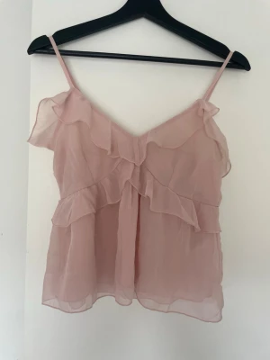 Ljusrosa volangtop från Nelly - Säljer en söt ljusrosa linnetopp från Nelly med tunna justerbara axelband och volangdetaljer fram och bak. Toppen är gjord i ett tunt, luftigt material. Perfekt att styla med jeans eller kjol för en trendig look. Aldrig kommit till användning så inga defekter, skriv vid frågor! 