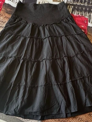 Svart volangkjol från H&M Mama - Säljer en svart långkjol från H&M Mama med flera volanglager. Kjolen har en bred, mjuk midjeresår och är perfekt för en avslappnad och bekväm stil. Tillverkad i mjukt bomullsmaterial som känns skönt mot huden.