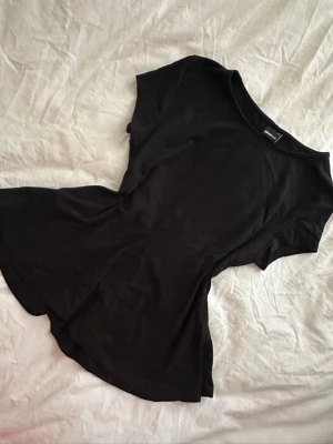 Svart peplum top - En svart peplum top med rund halsringning och korta ärmar. Tillverkad i mjuk bomull som känns skön mot huden. Perfekt till jeans eller kjol för en clean och avslappnad look.