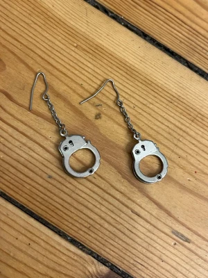Örhängen handbojor - Unika örhängen i form av små handbojor i silverfärgad metall. Nickel/oäkta.