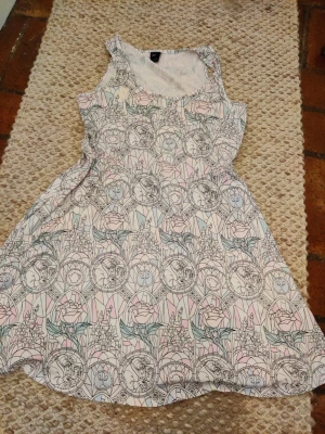 Mönstrad pastellfärgad klänning skönheten och odjuret Disney  - Säljer en söt klänning med pastellfärgat mönster i rosa, blått och grönt. Klänningen har ärmlös design, rund halsringning och ett unikt tryck med blommor och sagoinspirerade motiv. Perfekt för dig som gillar lekfulla och färgglada plagg. Köpte i usa i hottopic 