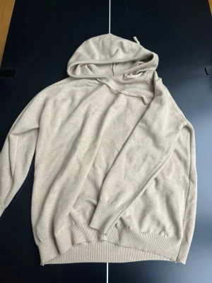 Beige hoodie i mjuk bomull - Snygg beige hoodie med huva och dragsko. Tillverkad i mjukt material med ribbade muddar vid ärmslut och nederkant. Perfekt för en avslappnad och stilren look.