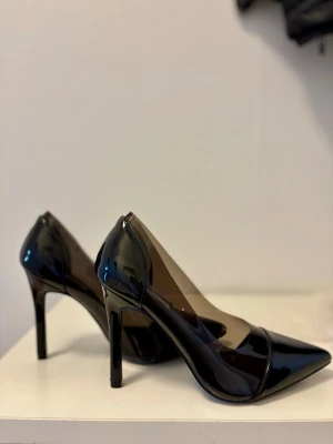 Svarta lackpumps med spetsig tå - Aldrig använda, nya utan prislapp eller box. Snygga svarta pumps med spetsig tå och hög klack. Skorna är i glansigt lackmaterial och har en klassisk, elegant design som passar perfekt till både dressade och trendiga outfits.