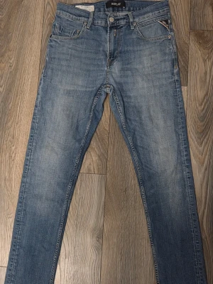Blå slim fit jeans från Replay - Snygga blå slim fit jeans från Replay med klassisk femficksdesign och diskreta slitningar framtill. Jeansen har normal midja, raka ben och är tillverkade i mjuk denim med lätt stretch för skön passform. Perfekta till en avslappnad stil.
