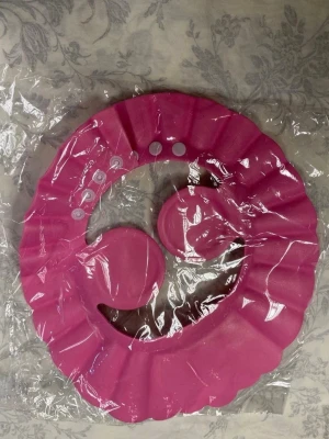 Barn duschhatt med öronskydd - En  duschhatt i plast med volangkant och inbyggda öronskydd. Hatten har justerbara tryckknappar för att passa olika huvudstorlekar och skyddar håret och öronen vid dusch eller bad. Finns olika färger kvar 